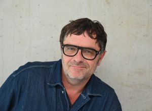 Zwei Perosnen sitzen in einem weißen raum, eine Frau mit braunem Haar und ein Mann mit Brille